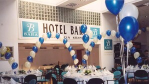 A hotel banquet hall with tables set for a formal event, featuring a blue and white balloon arch and a sign reading "HOTEL BARÁ". - Hotel Bara Junior (Budapest)