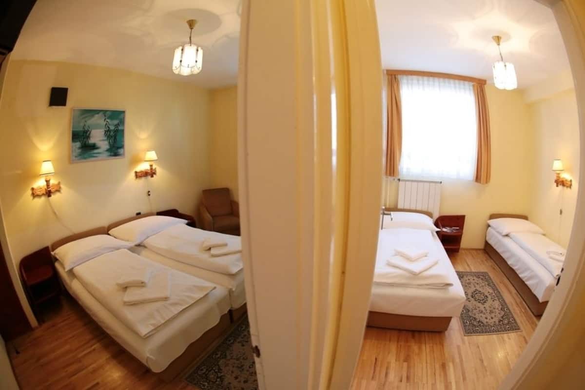A hotel room with two beds, a chair, a painting on the wall, and two wall-mounted lamps.