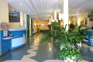A hotel lobby with a reception desk, potted plants, and a tiled floor. - Hotel Bara Junior (Budapest)