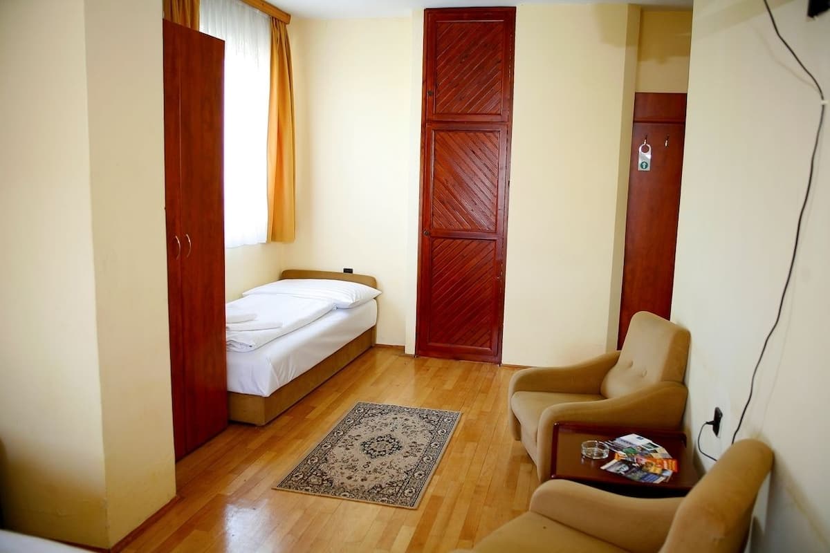 A small, single-room accommodation with a bed, a chair, a table, and a wardrobe.