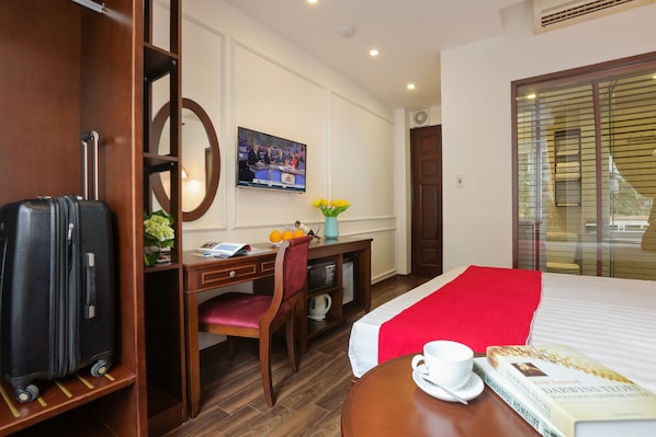A hotel room with a bed, a desk, a chair, a TV, a suitcase, a vase with flowers, and a book. - Hanoi La Vision Hotel (Hanoi)