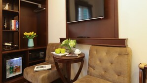 A living room with a flat-screen TV mounted on the wall, a small table with a vase of flowers, a sofa, and a mini-fridge. - Hanoi La Vision Hotel (Hanoi)