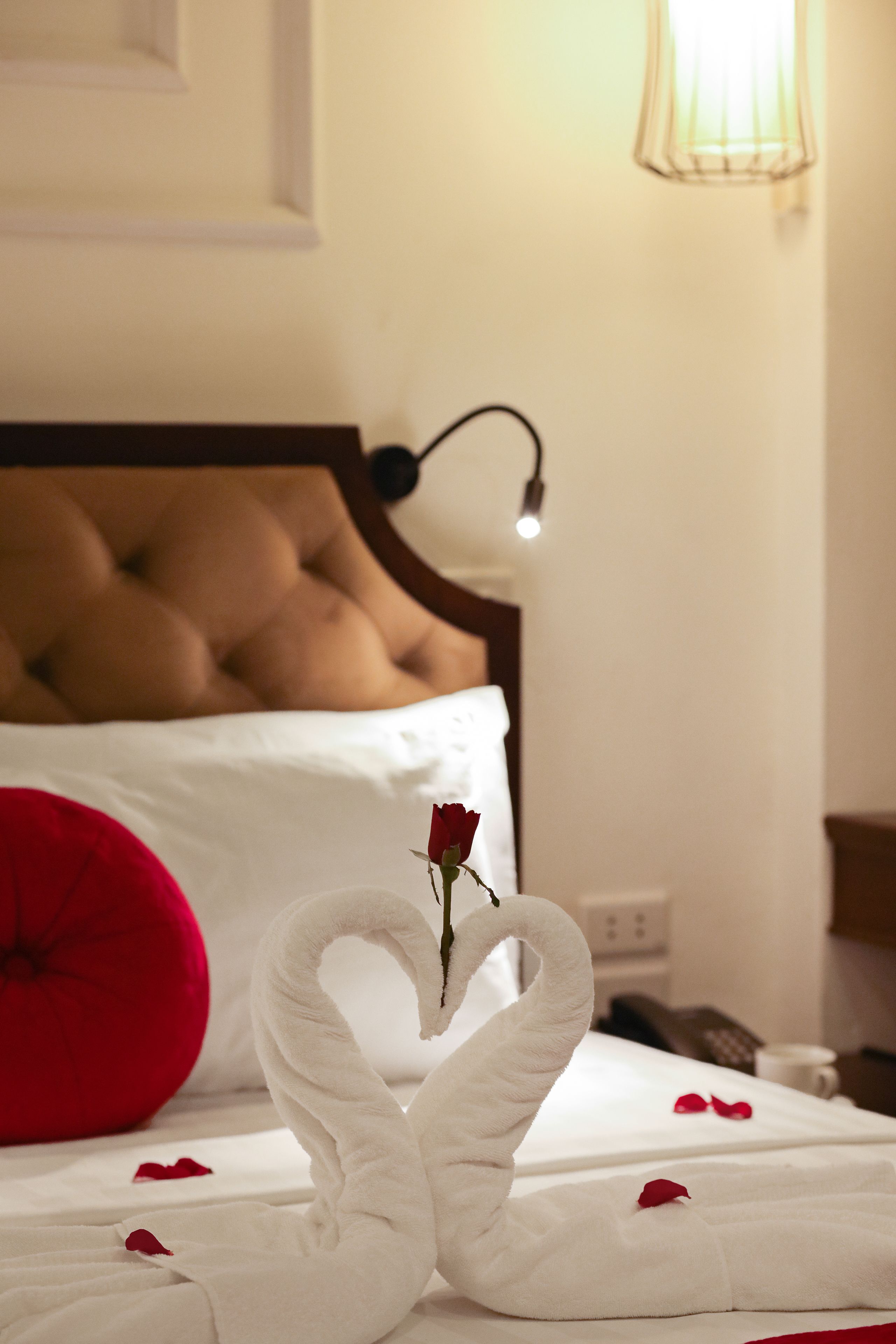 A bed with a swan towel arrangement and a single rose.
