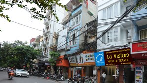 A street view with a hotel named La Vision Hotel & Travel, featuring a signboard with contact details and a travel office. - Hanoi La Vision Hotel (Hanoi)