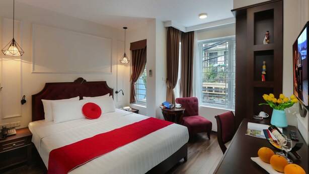 A hotel room with a bed, a desk with a vase of flowers, a chair, and a window with curtains. - Hanoi La Vision Hotel (Hanoi)