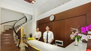 A reception desk with a clock, a staircase, and a decorative orchid arrangement. - Hanoi La Vision Hotel (Hanoi)