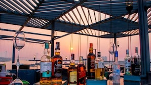 Zona de bar con diferentes botellas de licor y vasos, con vista al atardecer de fondo.