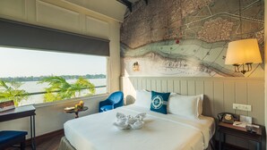 Habitación de hotel con una cama grande, un mapa en la pared, vistas al agua y un escritorio con una silla.