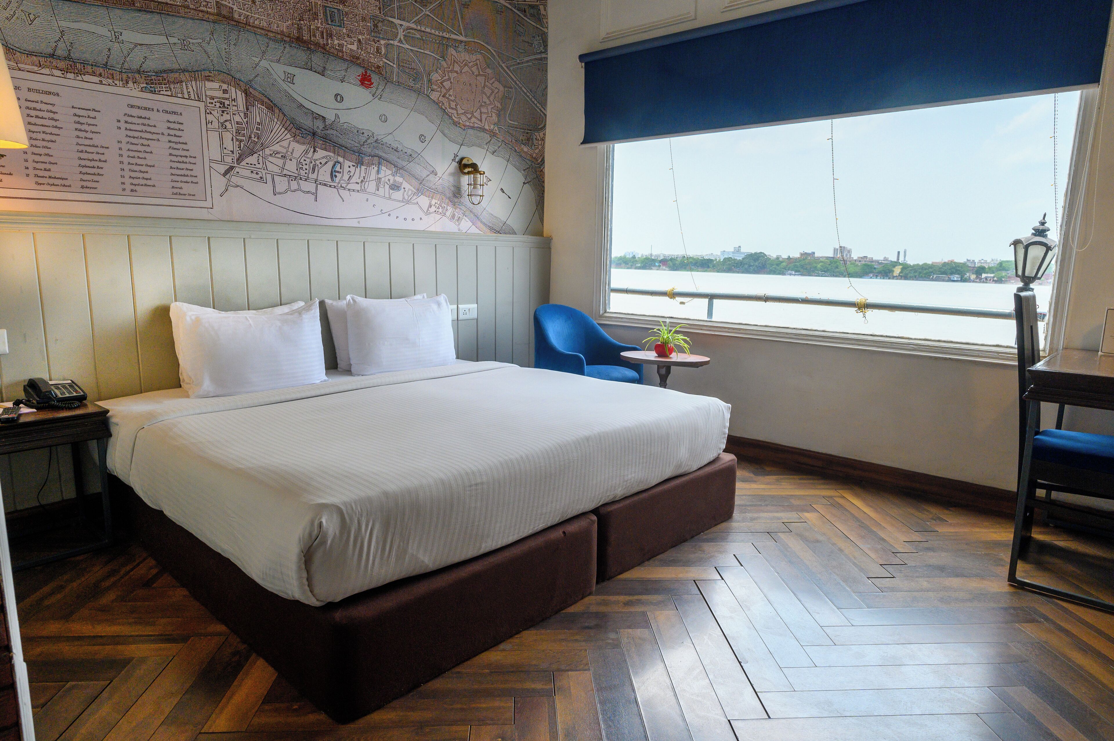 A hotel room with a large bed, a map on the wall, a view of a river, and a small table with a plant.