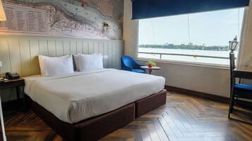 A hotel room with a large bed, a map on the wall, a view of a river, and a small table with a plant.