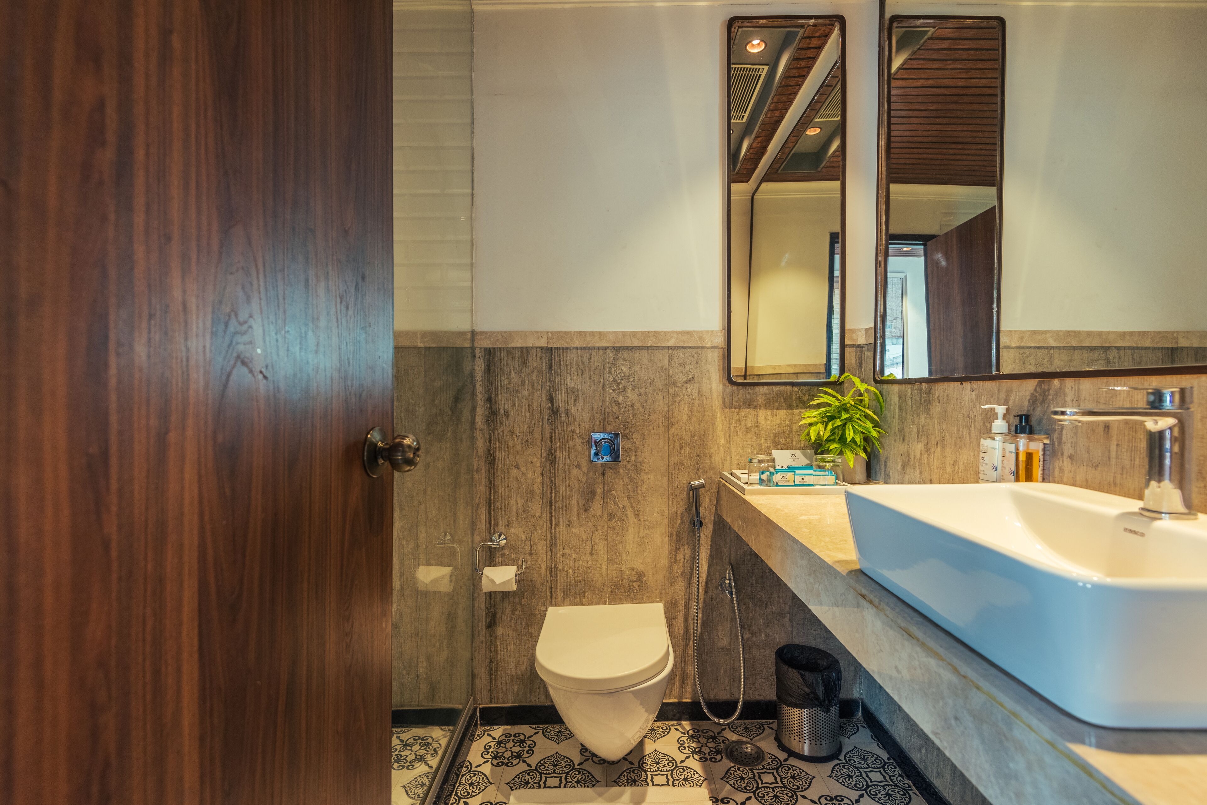A modern bathroom with a wooden door, a toilet, a sink, a mirror, and a shower.