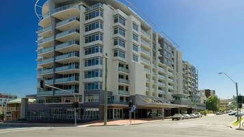 A multi-story hotel with balconies, a covered entrance, and a clear blue sky.