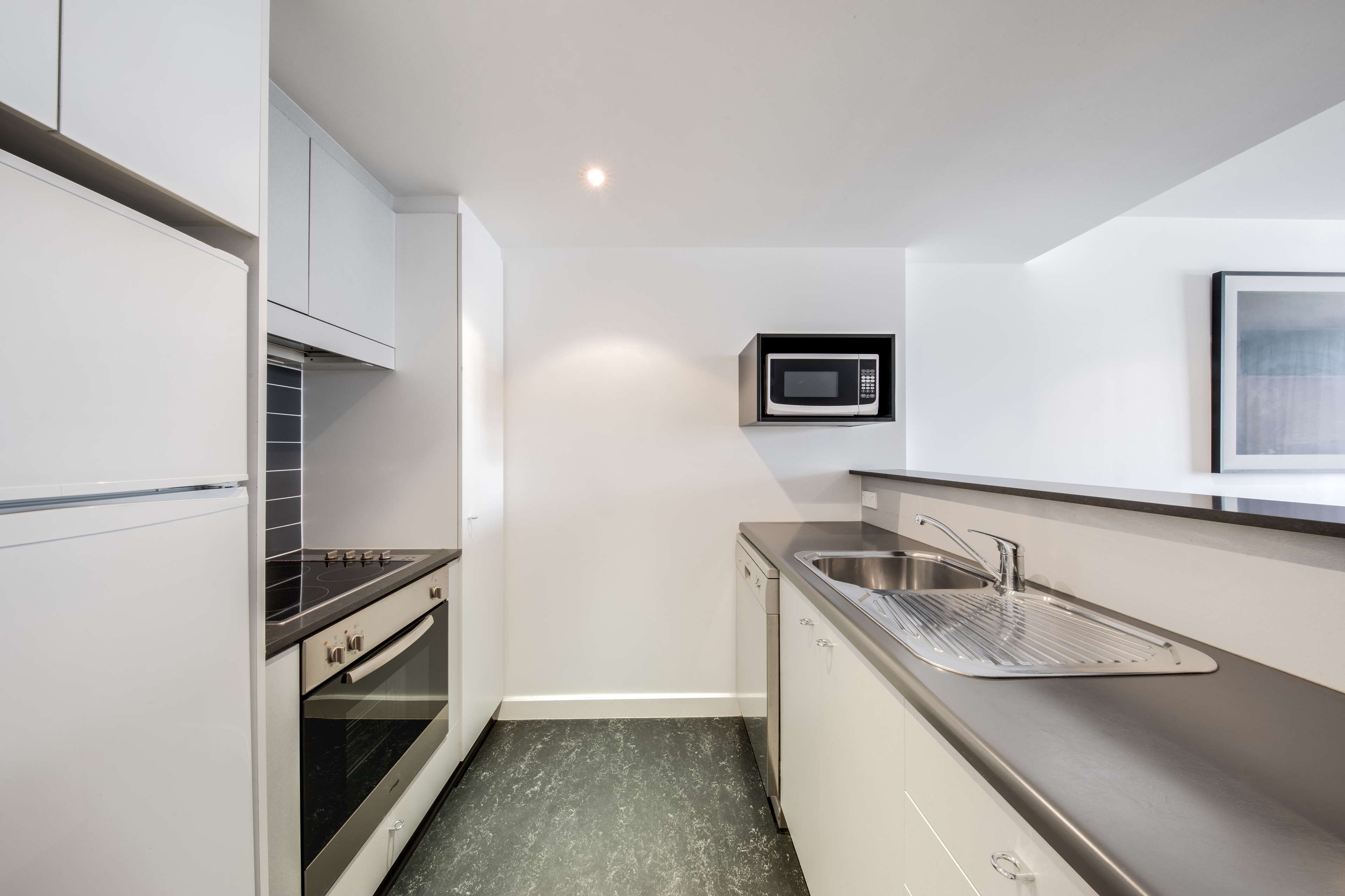 A compact kitchen with white cabinetry, a stainless steel sink, a microwave, and a built-in oven.