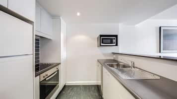 A compact kitchen with white cabinetry, a stainless steel sink, a microwave, and a built-in oven.