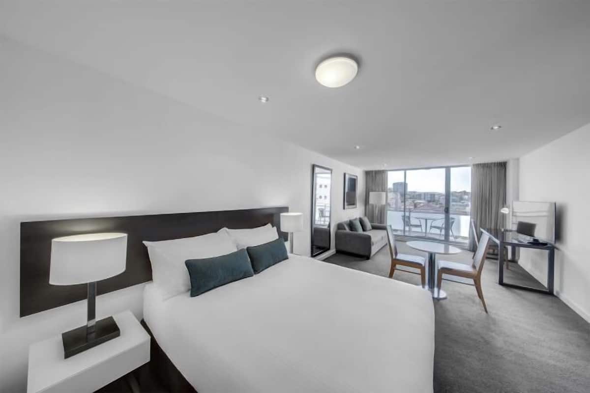 Ett modernt hotellrum med en stor säng, ett skrivbord, en stol och utsikt över staden.