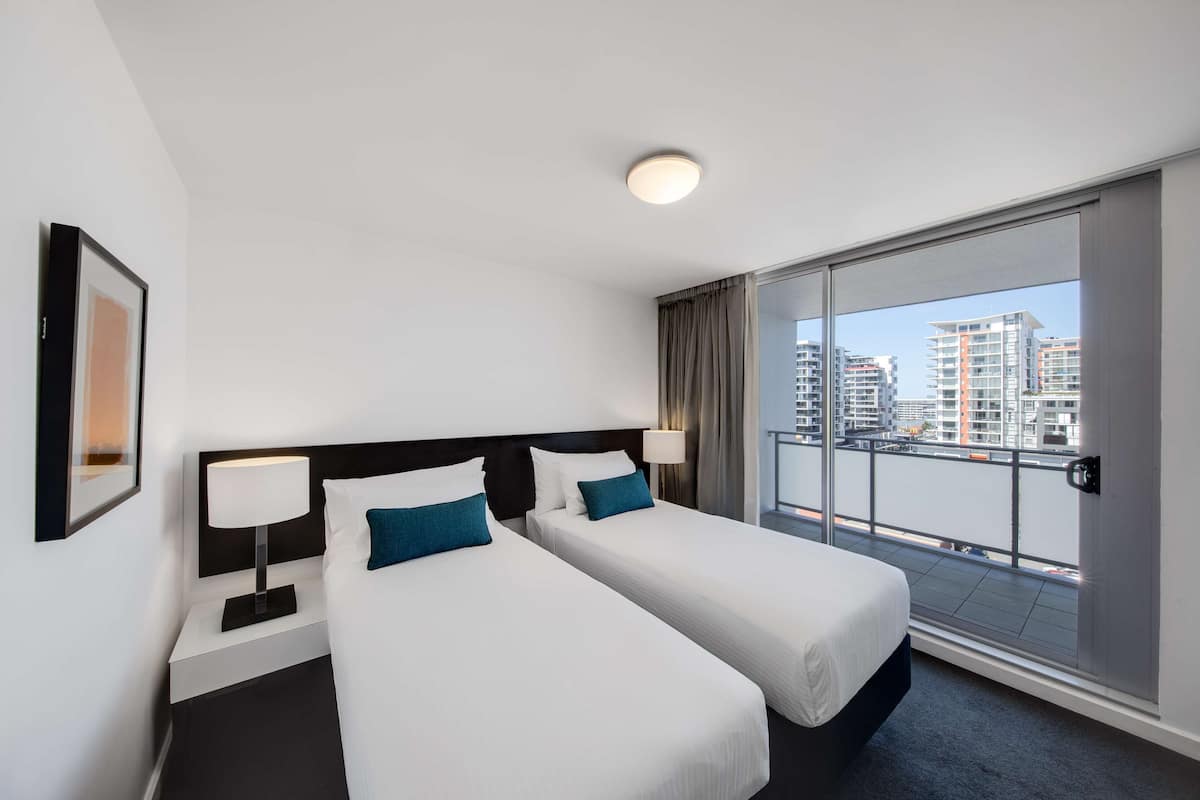 Ett hotellrum med två sängar, ett stort fönster med utsikt över staden och en taklampa.