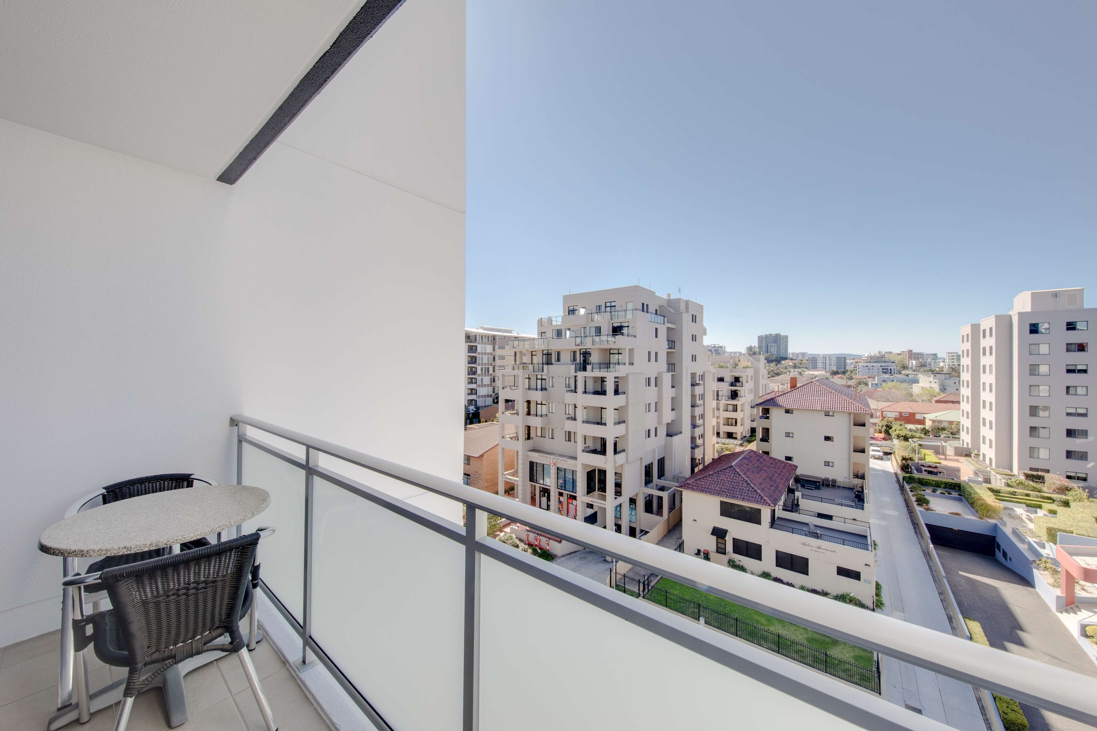 A balcony with a table and chairs, overlooking a residential area with modern buildings.