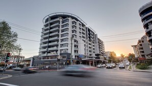 Monikerroksinen rakennus, jossa on kaareva julkisivu, useita parvekkeita ja katutasossa sijaitseva liiketila.
