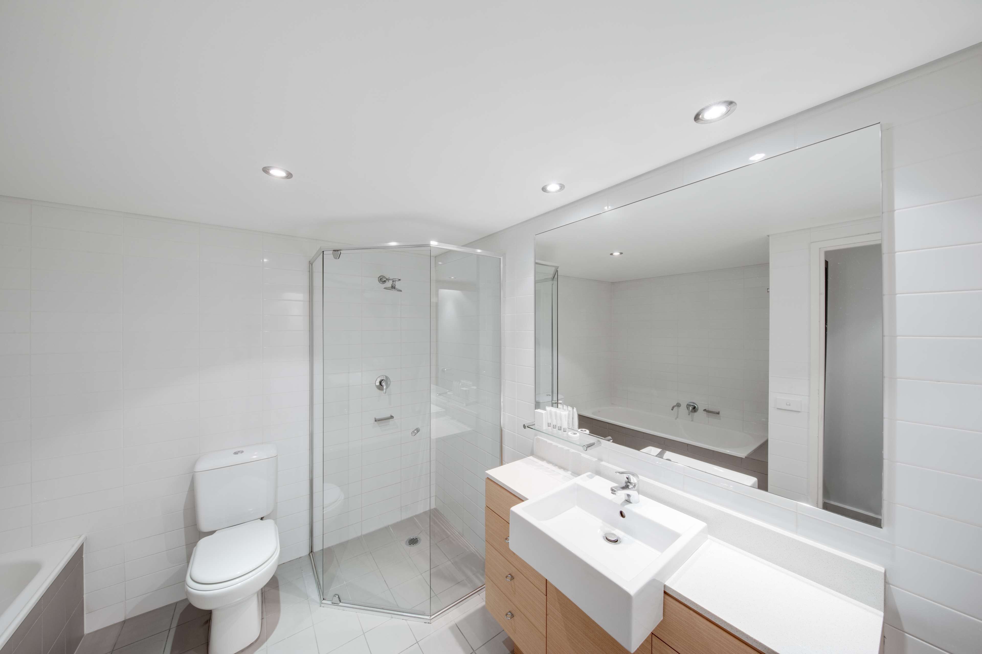 Une salle de bain moderne avec une douche à parois de verre, des toilettes blanches et un meuble-lavabo doté de deux vasques.