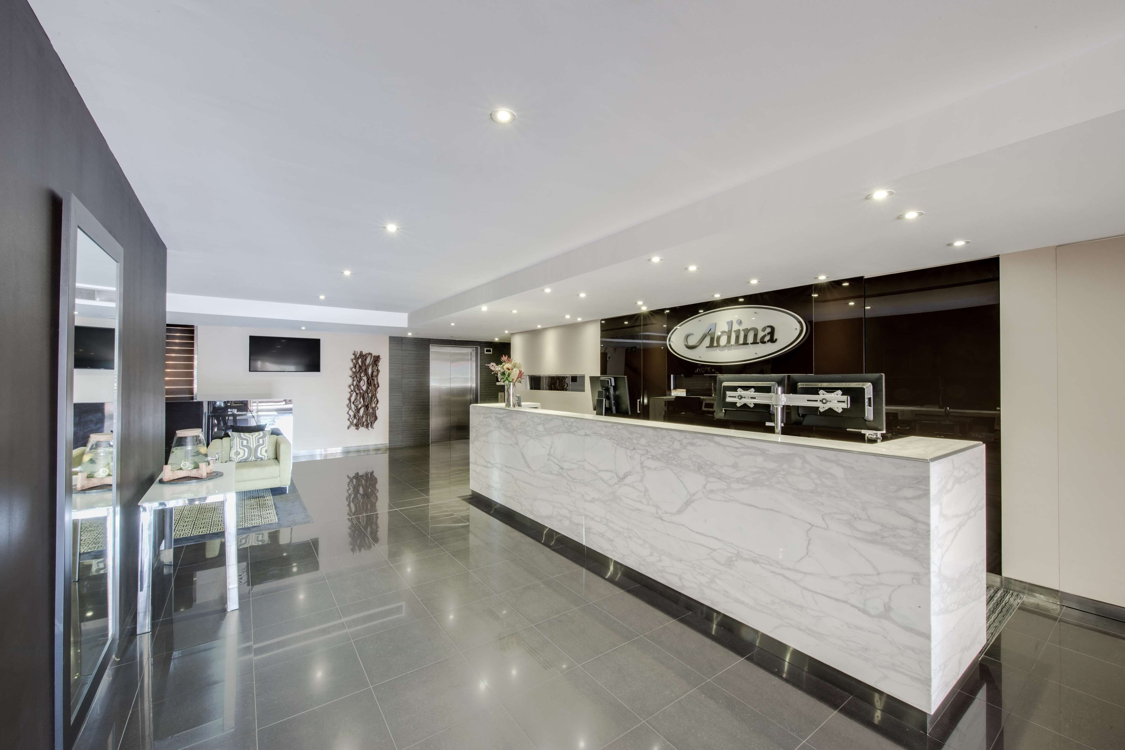 A modern reception area with a marble counter, a sign reading "Adina," and a glass partition.