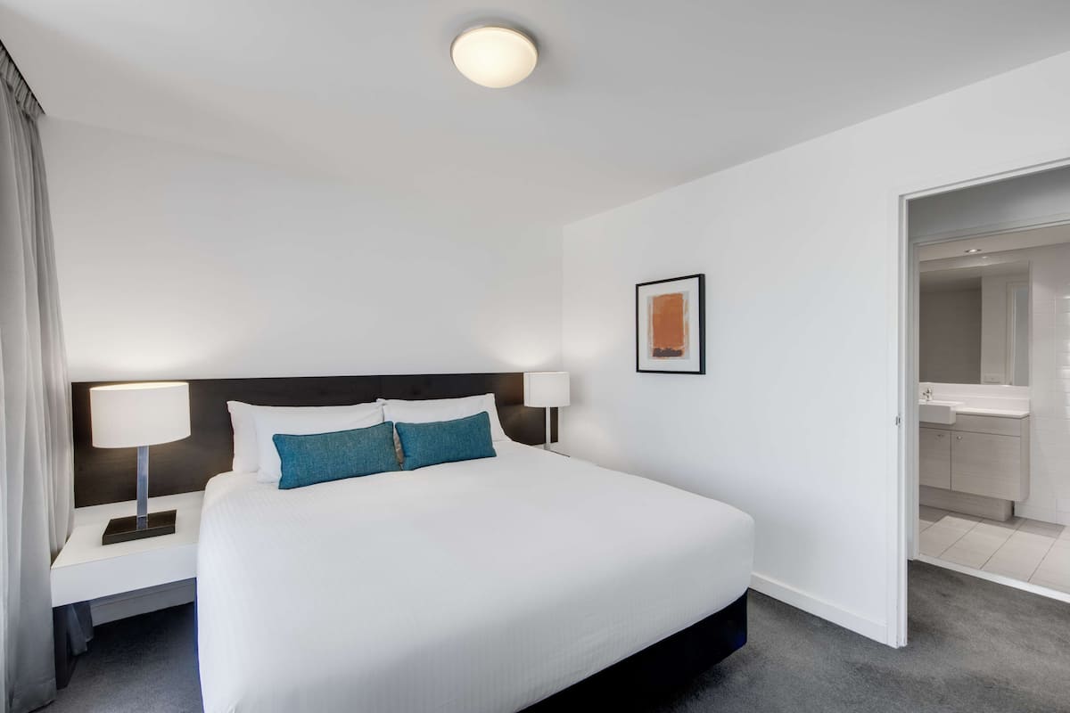 Ett hotellrum med en stor säng, två sängbord med lampor, en inramad tavla på väggen och en öppen dörr till badrummet.