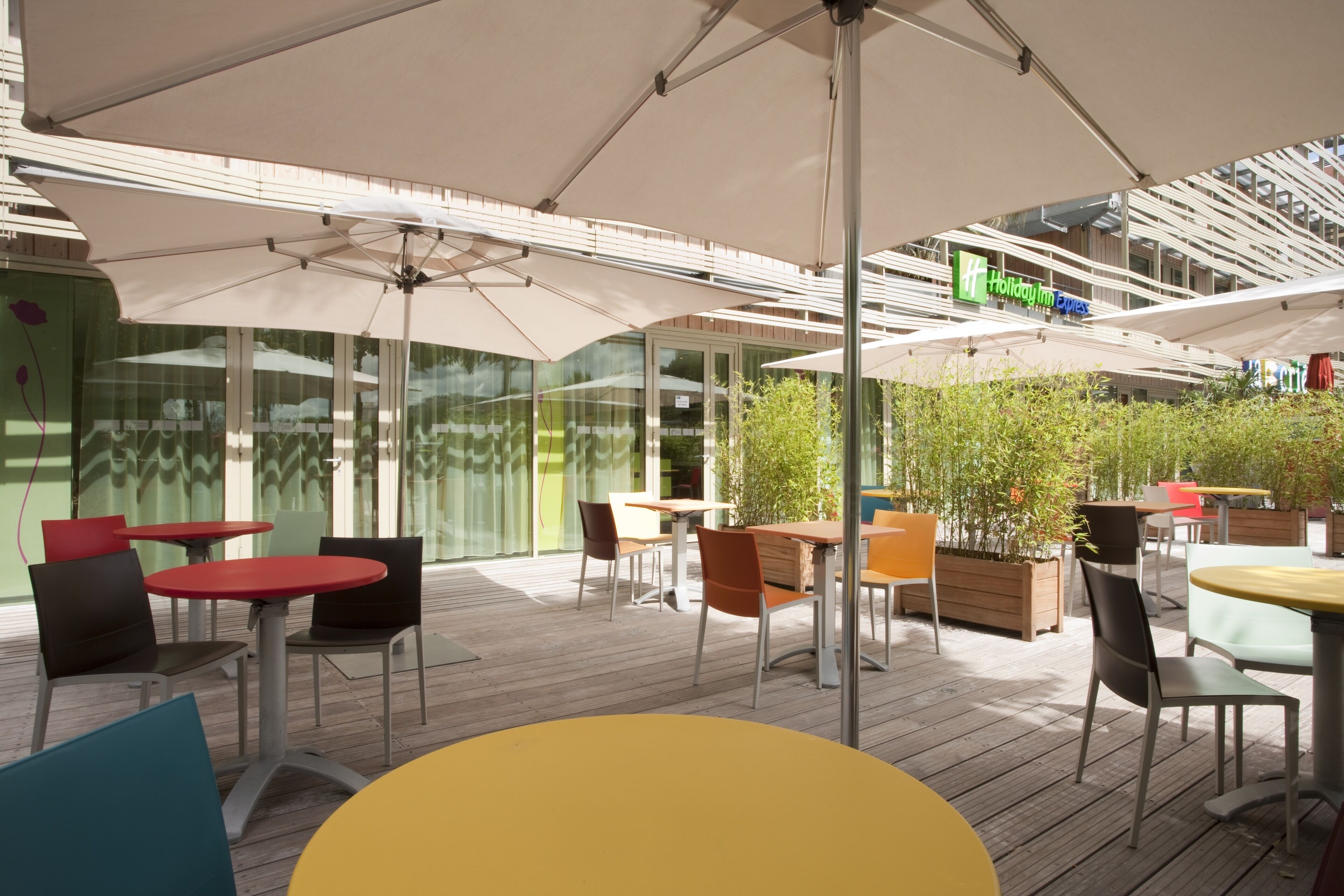 Un patio al aire libre con varias mesas y sillas, un letrero de Holiday Inn Express y una pared de vidrio con reflejos.