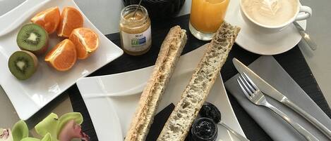 Un desayuno con pan, fruta, mermelada, mantequilla y una taza de café.