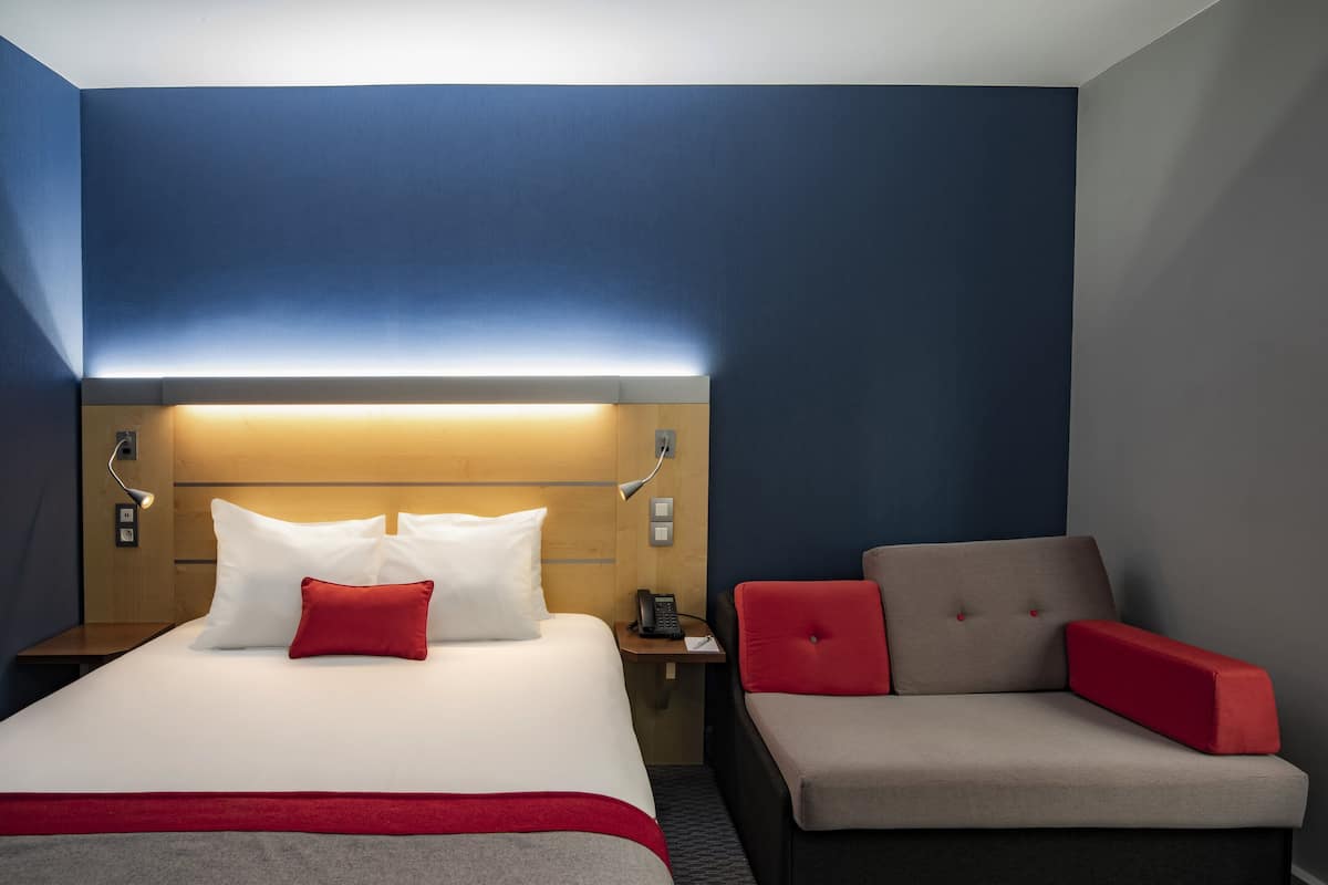 A hotel room with a bed, a nightstand, a desk, and a sofa.