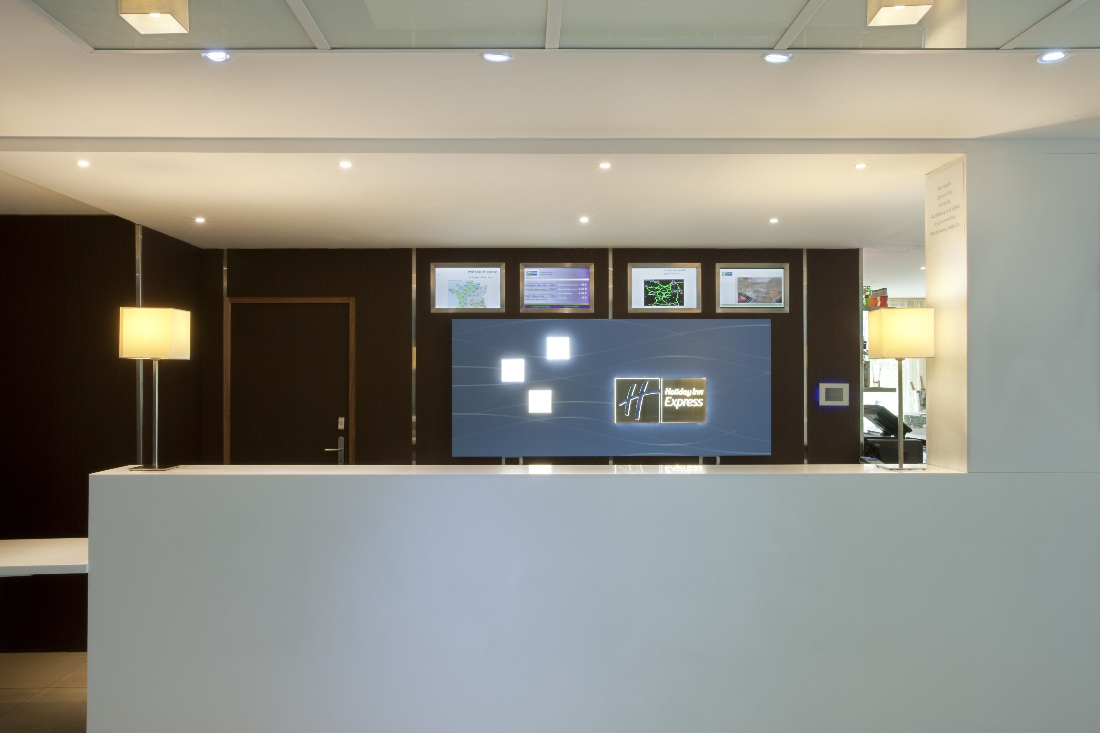 A modern reception desk with digital displays, a flat-screen TV, and a logo for Holiday Inn Express.