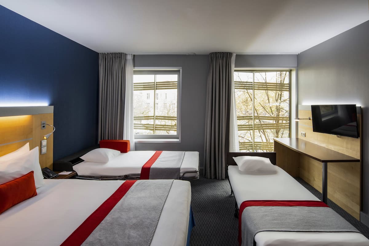 A hotel room with two beds, a TV, and large windows.