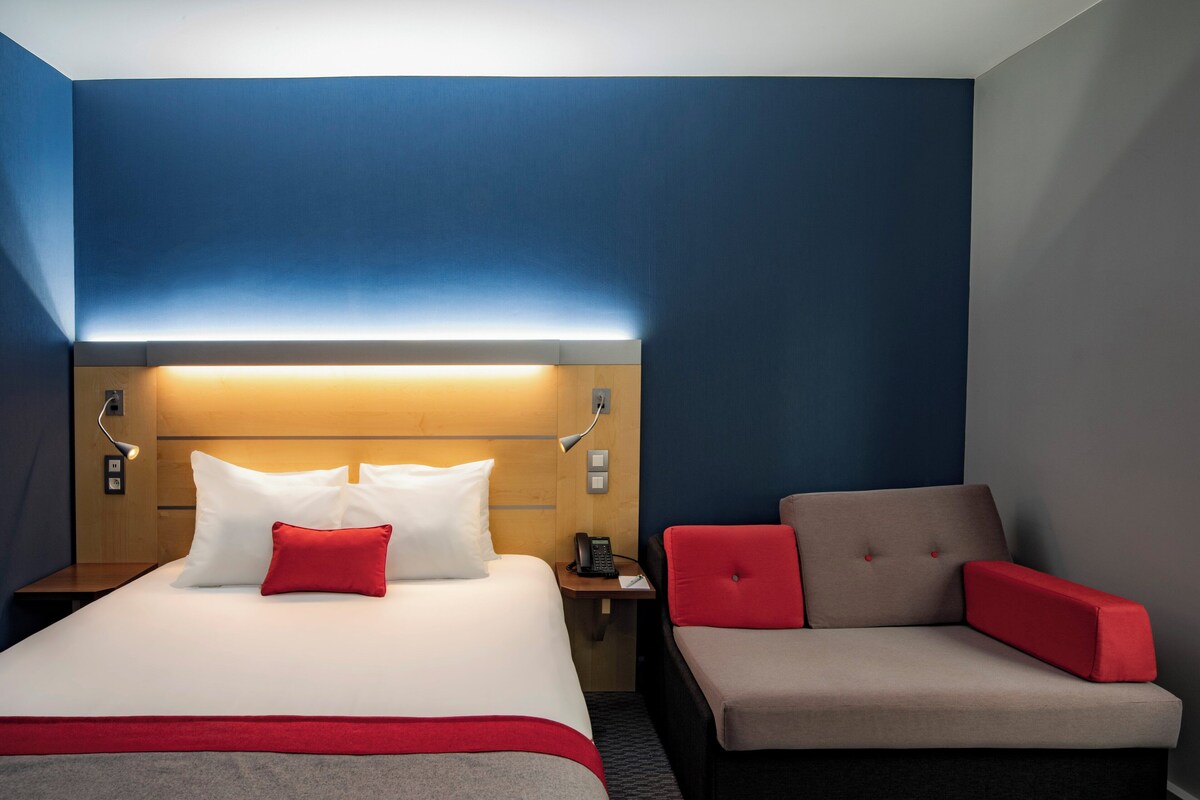 A hotel room with a bed, a nightstand, a desk, and a sofa.