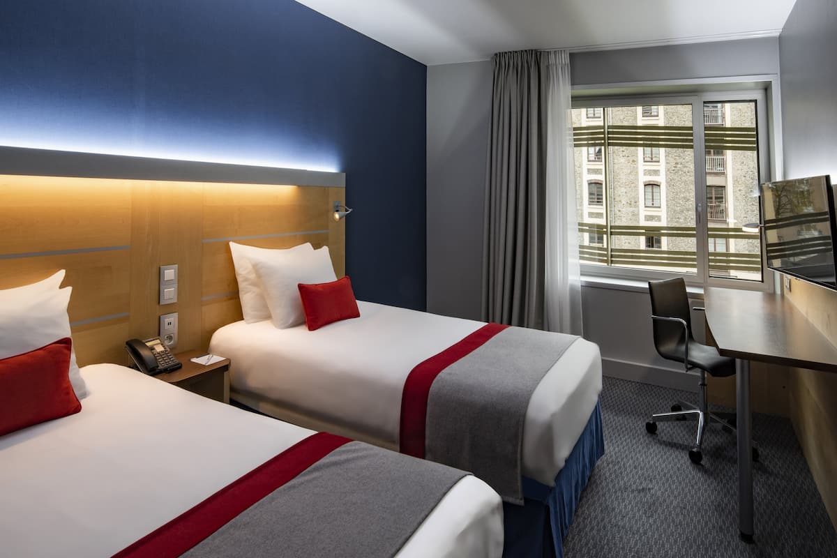 A hotel room with two beds, a desk, a chair, a telephone, and a window with curtains.