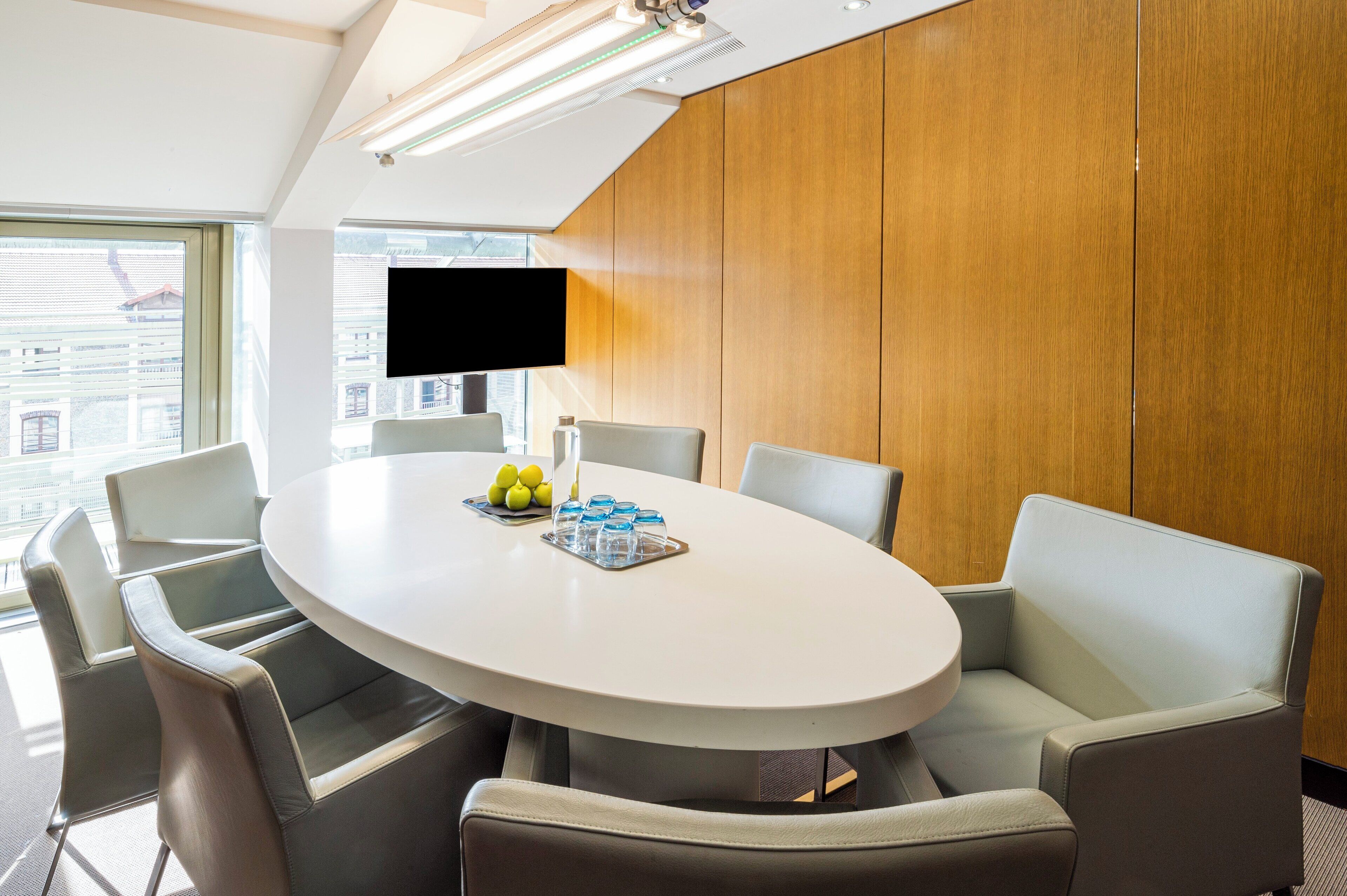 A conference room with a round table, six chairs, a flat-screen TV, and a wooden wall.
