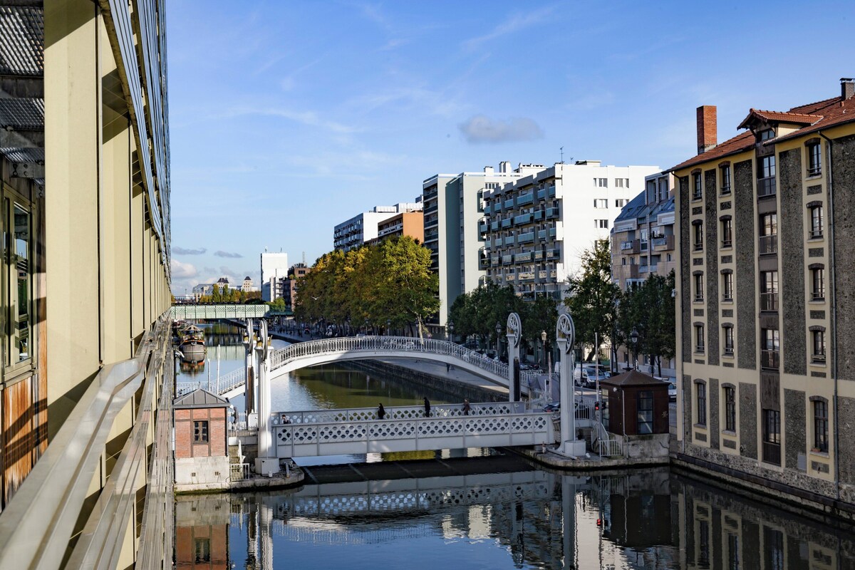 A canal with a white bridge, surrounded by buildings with balconies and a clear sky.