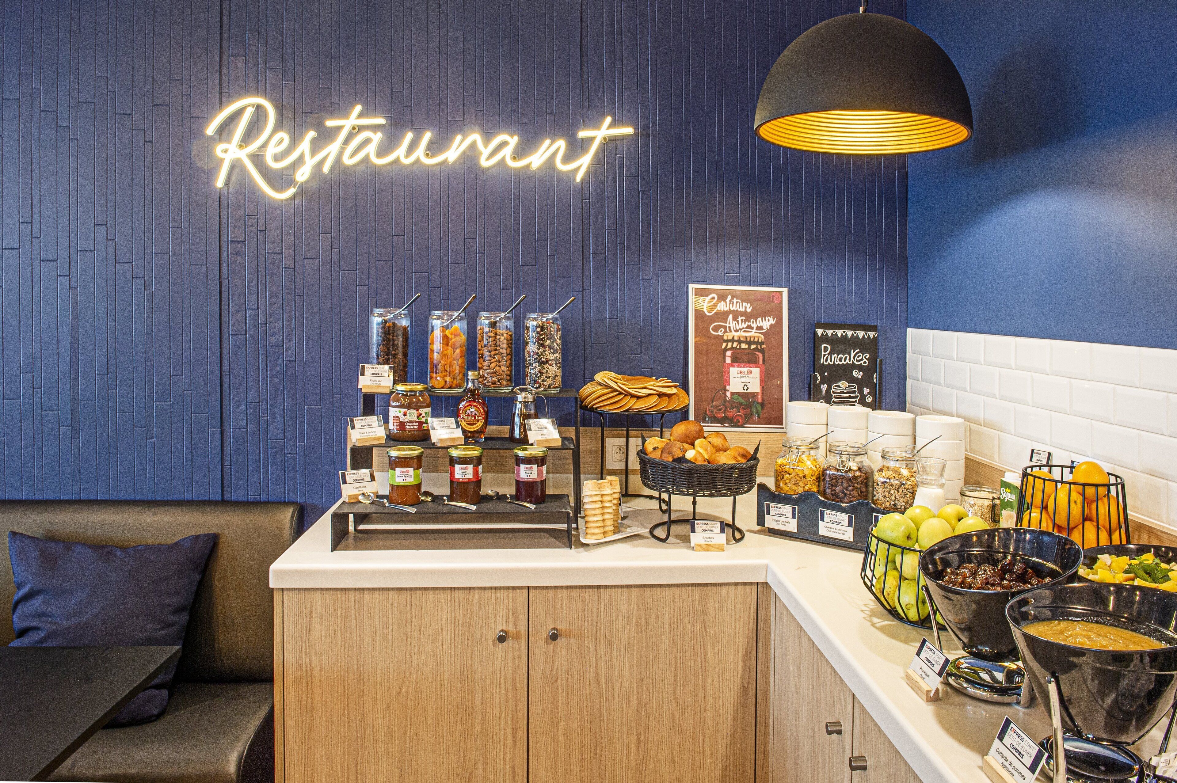 A restaurant counter with a neon sign, various food items, and a seating area with a couch and pillows.