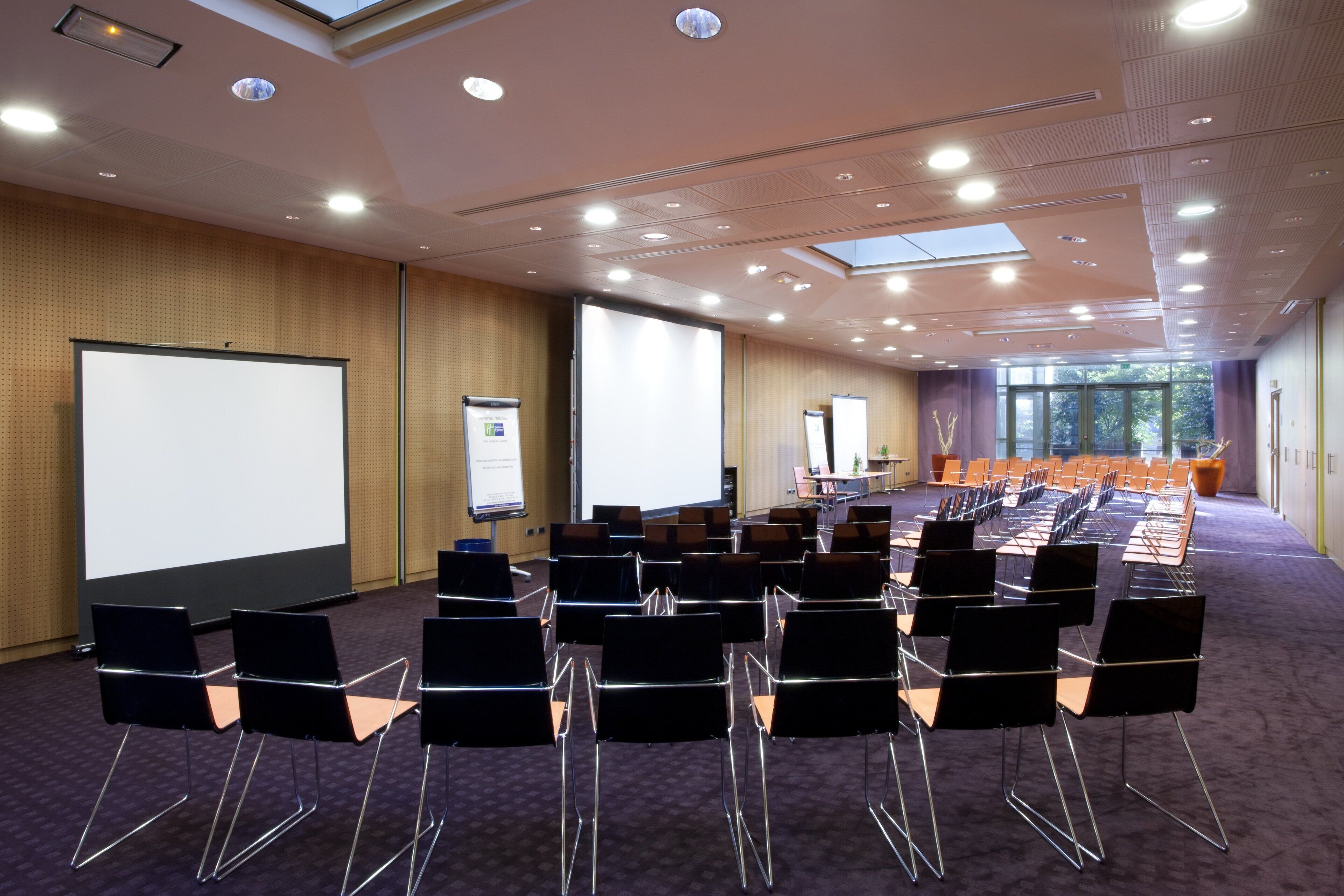 Ein Konferenzraum mit Reihen von Stühlen, einem großen Bildschirm und einer Tafel.
