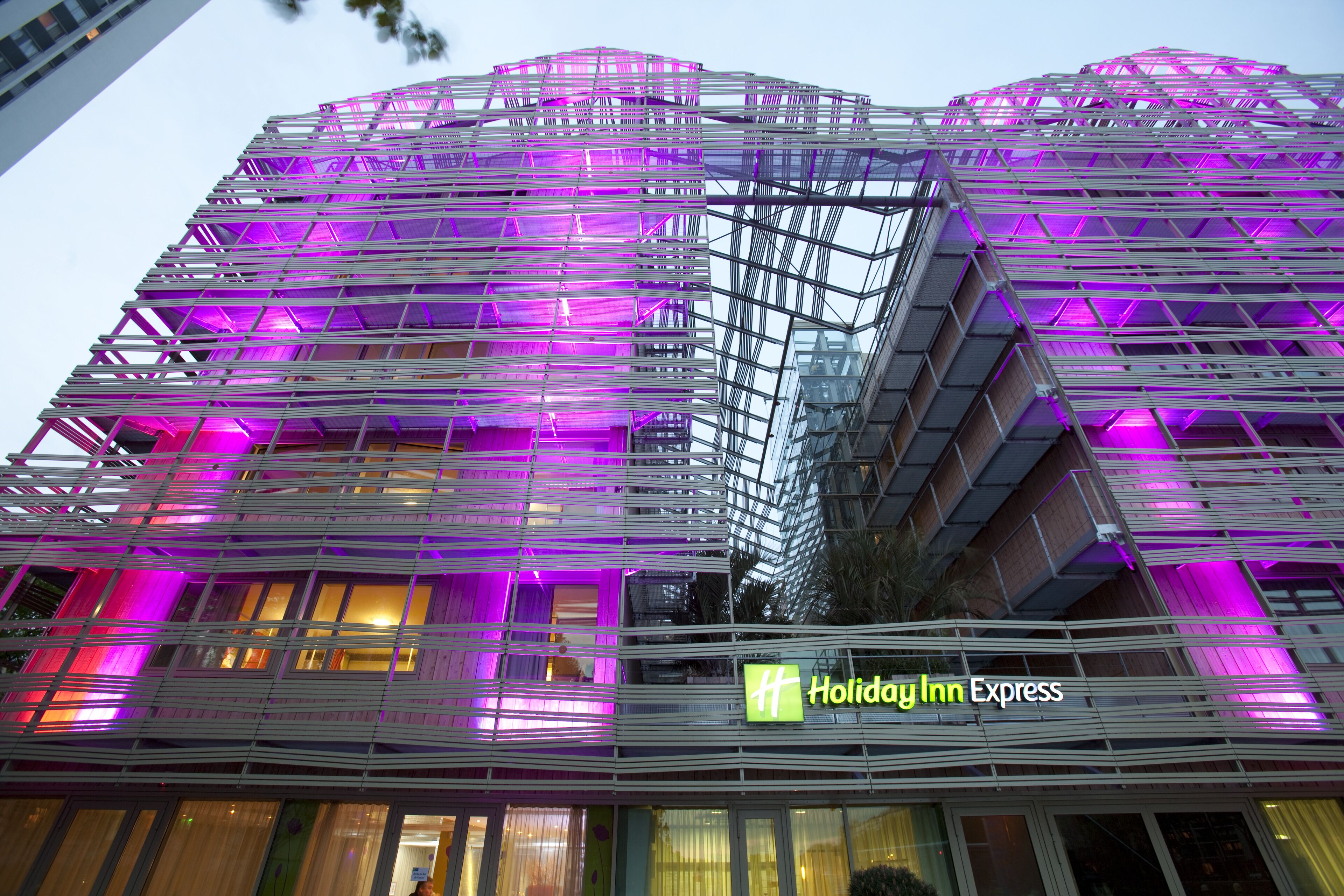 Edificio Holiday Inn Express con un design architettonico moderno caratterizzato da una facciata a griglia e illuminazione dai toni viola.