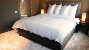 Een opgemaakt bed met een grijs hoofdeinde, een nachtkastje met een lamp en een vloerbedekking.