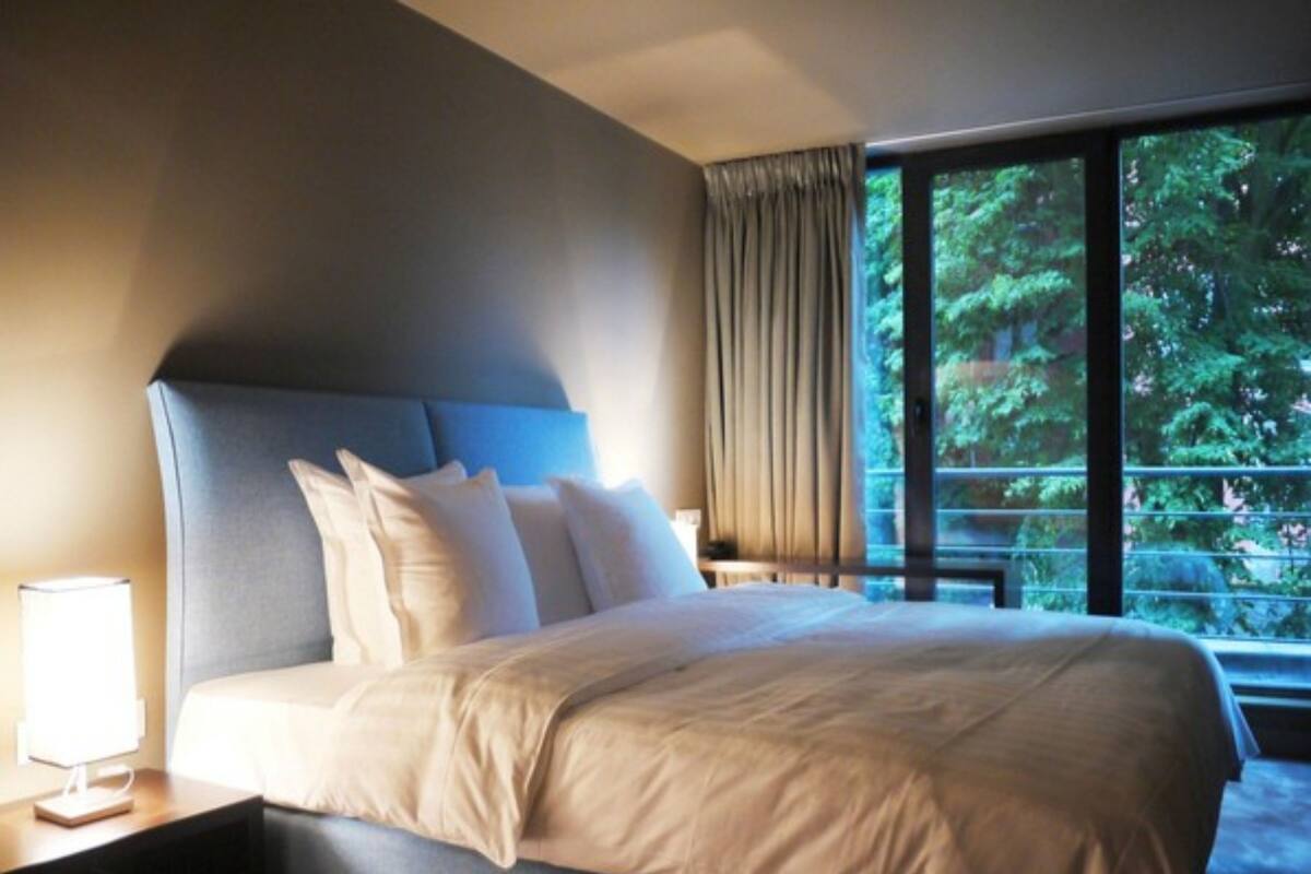 A hotel room with a large bed, a nightstand, a lamp, and a window with a view of trees.
