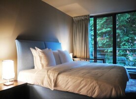 A hotel room with a large bed, a nightstand, a lamp, and a window with a view of trees.
