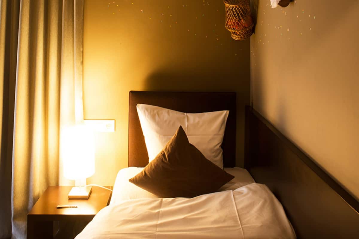 A neatly made bed with white and brown pillows, a bedside lamp, and a small table with a remote control.