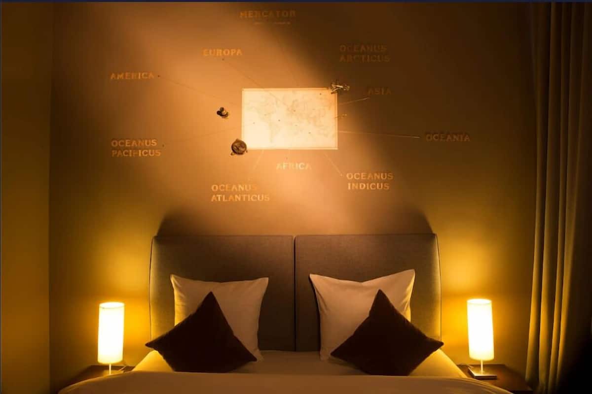 A hotel room with a large bed, two bedside lamps, and a wall map highlighting continents and oceans.