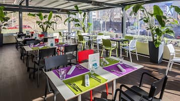 Un restaurante con terraza, mesas con individuales verdes y grandes macetas.
