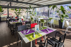 Ein Restaurant mit Außenbereich, Tischen mit grünen Tischsets und großen Kübelpflanzen.