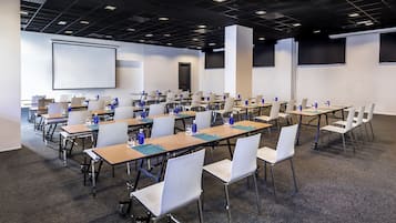 Un salón de conferencias con varias mesas y sillas, equipado con computadoras portátiles, botellas de agua y vasos.