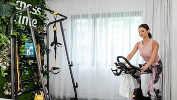 Een vrouw gebruikt een hometrainer in een kamer met een groene wand en een groot raam.