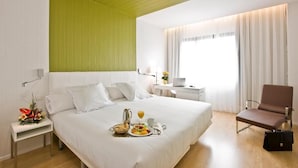 Habitación de hotel con una cama grande, un escritorio, una silla y una bandeja de desayuno sobre la cama.