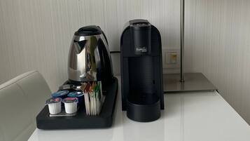 Una camera d'albergo con un tavolo bianco, una macchina per il caffè nera, un bollitore d'argento e un vassoio con diversi oggetti.