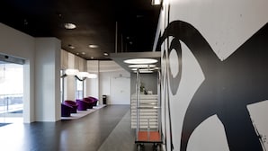 Un interior moderno con un largo pasillo, una zona de estar con sillas moradas, un carrito con una planta y una gran obra de arte en la pared.