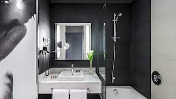 Une salle de bain moderne avec un grand miroir, un lavabo blanc, une douche et un porte-serviettes.